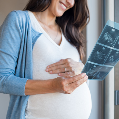 Pregnant woman holding her bump beside ultrasound scan images
