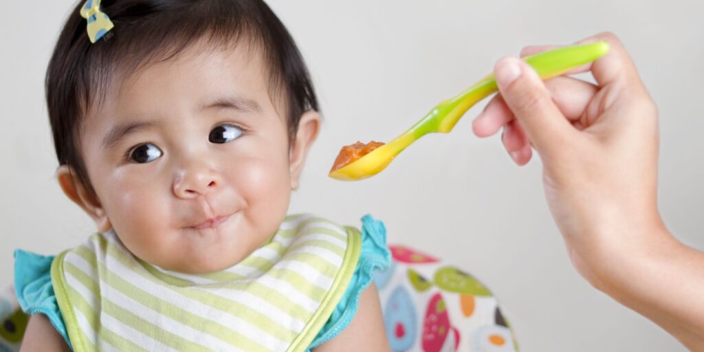 Baby in a bib turning away from a spoonful of food