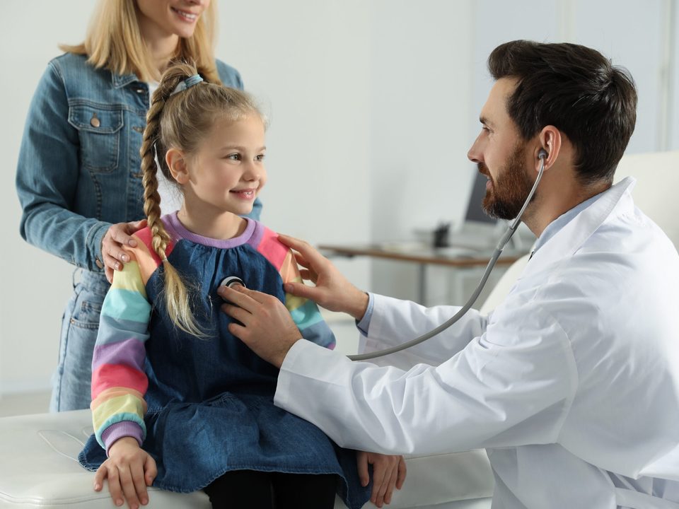 A paediatrician gently examining a smiling child with a stethoscope